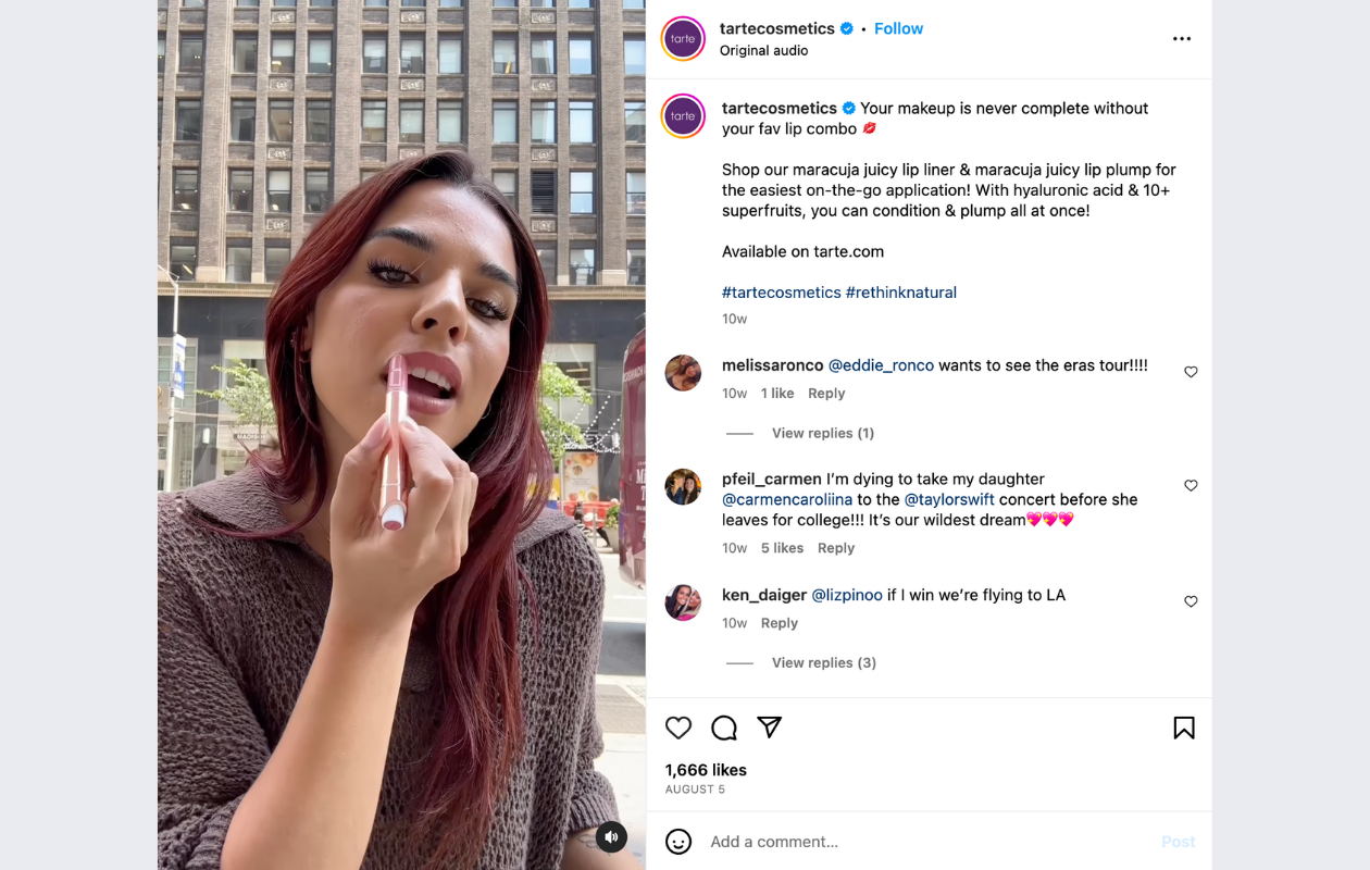 screenshot from tarte cosmetics insta with a girl applying listick, wearing a brown sweater, near a tall building